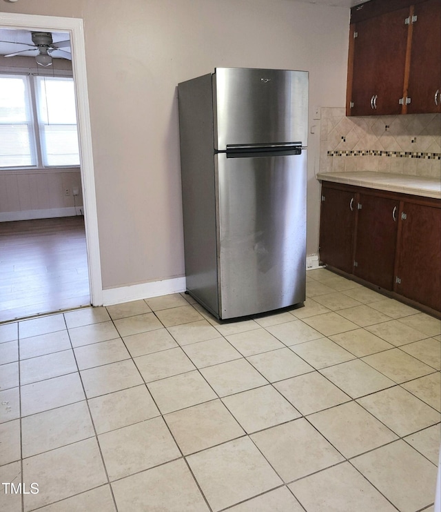 kitchen featuring stainless steel fridge, backsplash, light tile patterned floors, dark brown cabinets, and ceiling fan