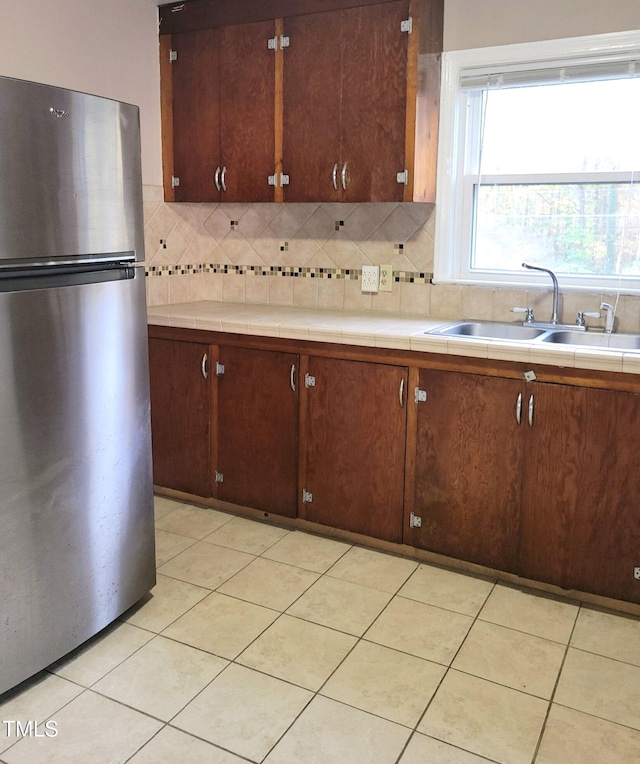 kitchen featuring tile countertops, backsplash, sink, and stainless steel fridge