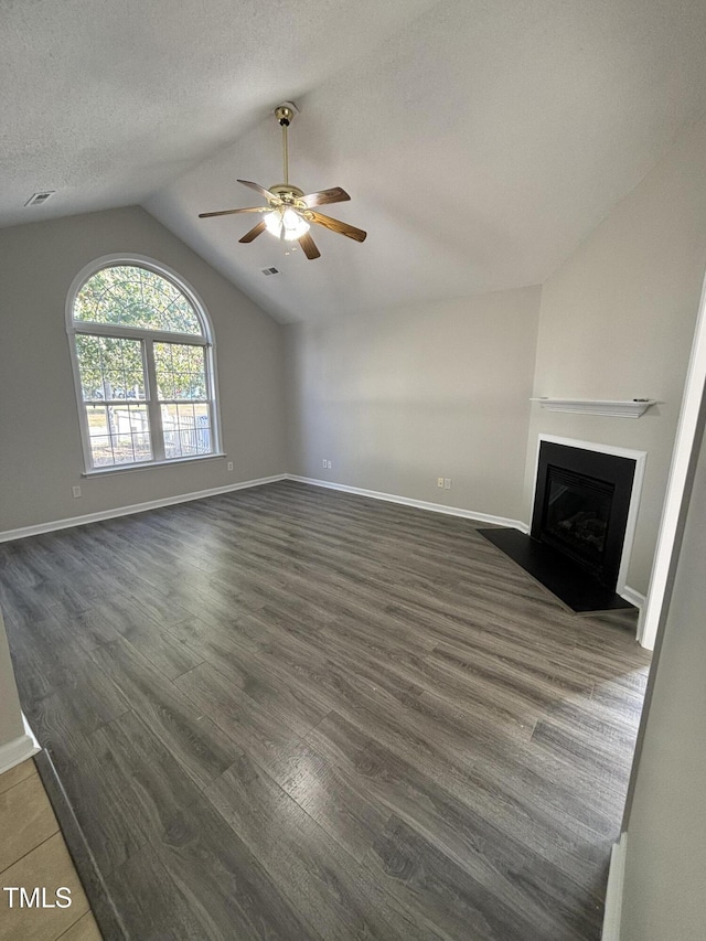 unfurnished living room featuring ceiling fan, vaulted ceiling, dark wood finished floors, a fireplace with flush hearth, and baseboards