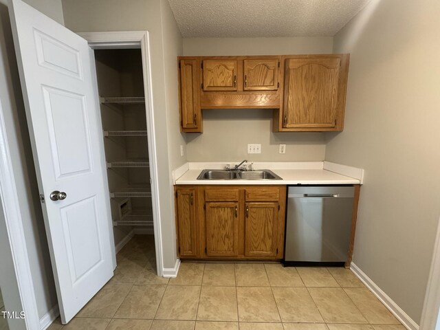 kitchen featuring stainless steel dishwasher, a sink, light countertops, brown cabinets, and a textured ceiling