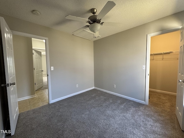 unfurnished bedroom with a walk in closet, carpet, a textured ceiling, a closet, and a ceiling fan
