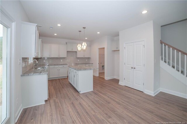 kitchen with hardwood / wood-style floors, a center island, sink, decorative light fixtures, and white cabinetry