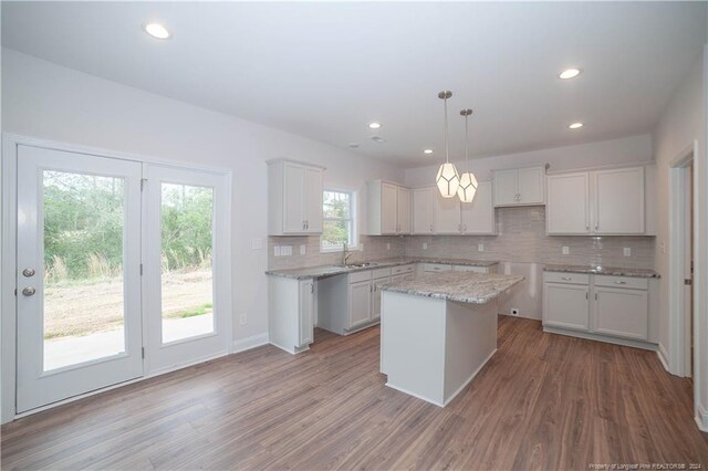 kitchen featuring white cabinetry, backsplash, decorative light fixtures, a kitchen island, and hardwood / wood-style flooring