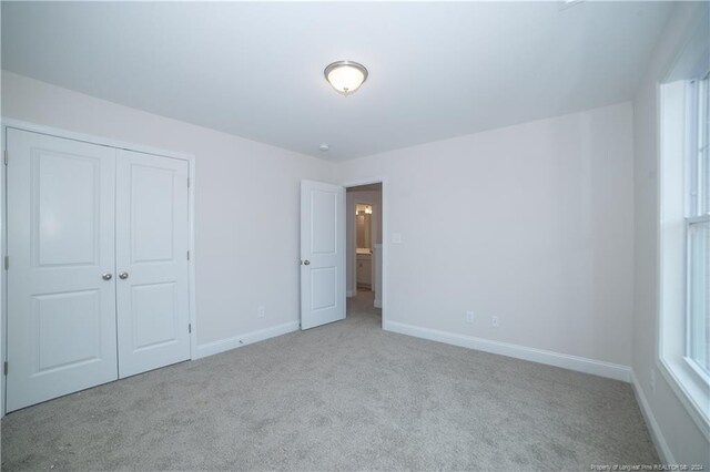 unfurnished bedroom featuring multiple windows, light carpet, and a closet