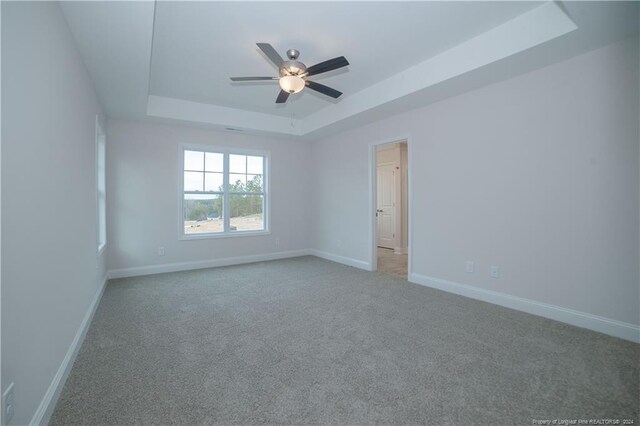 empty room featuring carpet, a tray ceiling, and ceiling fan