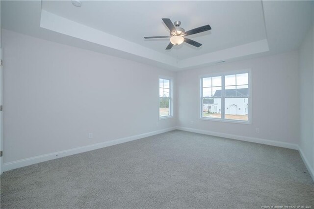 carpeted empty room with a raised ceiling and ceiling fan