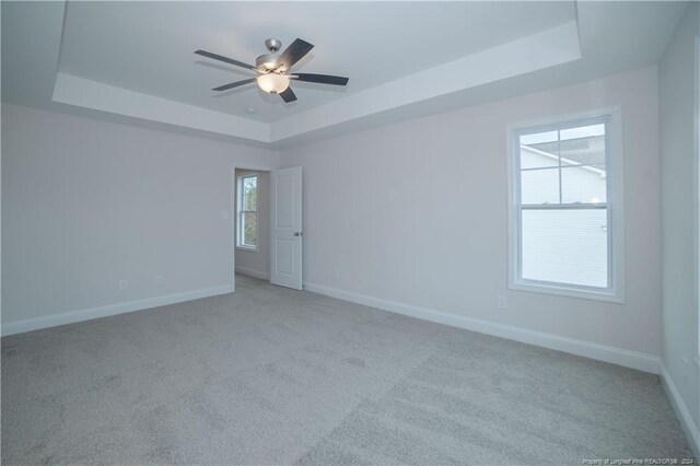 carpeted spare room featuring a tray ceiling and ceiling fan