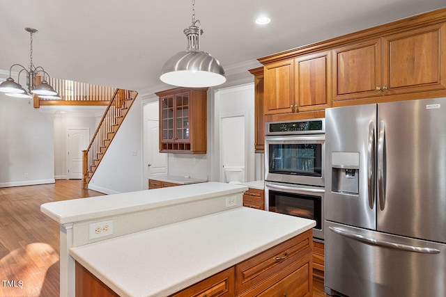 kitchen with hanging light fixtures, stainless steel appliances, crown molding, a center island, and light wood-type flooring