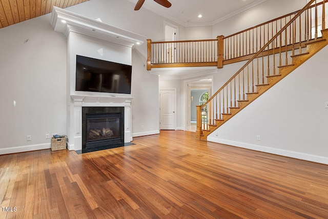 unfurnished living room featuring ornamental molding, hardwood / wood-style floors, a towering ceiling, and ceiling fan