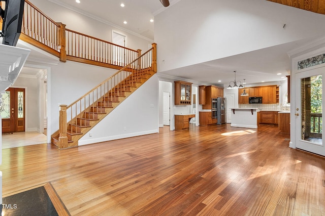 unfurnished living room featuring a chandelier, light wood-type flooring, a towering ceiling, crown molding, and french doors