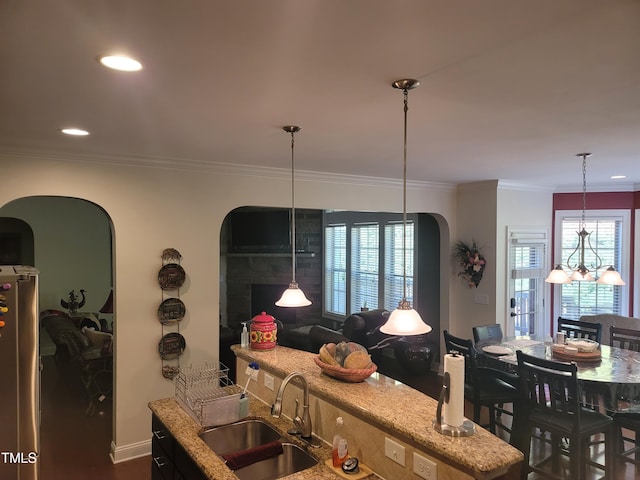 kitchen featuring sink, hanging light fixtures, a notable chandelier, stainless steel refrigerator, and light stone counters