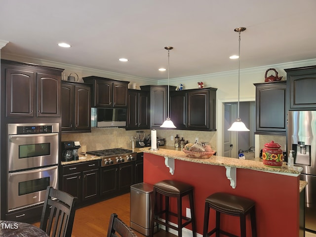 kitchen featuring appliances with stainless steel finishes, backsplash, decorative light fixtures, a kitchen breakfast bar, and light stone counters