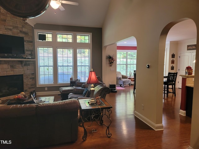 living room featuring ceiling fan, dark hardwood / wood-style floors, lofted ceiling, and a stone fireplace