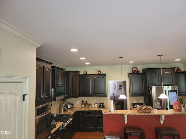 kitchen featuring light stone countertops, pendant lighting, appliances with stainless steel finishes, crown molding, and a breakfast bar area