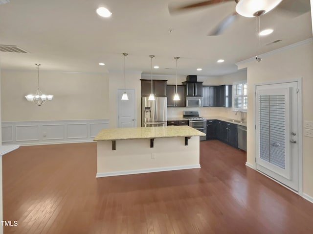 kitchen featuring dark wood-type flooring, appliances with stainless steel finishes, decorative light fixtures, and a kitchen island