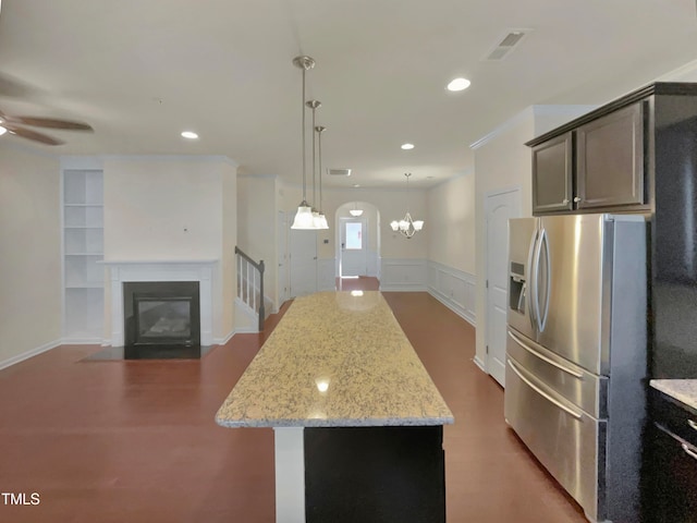 kitchen with light stone counters, stainless steel fridge with ice dispenser, a kitchen island, and hanging light fixtures