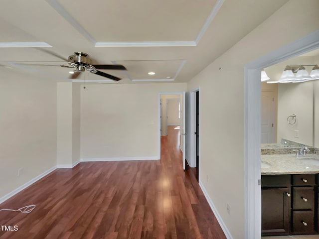 interior space with a raised ceiling, ceiling fan, dark wood-type flooring, crown molding, and sink