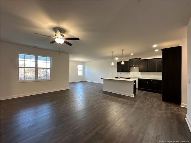 kitchen with an island with sink, sink, hanging light fixtures, ceiling fan, and dark wood-type flooring