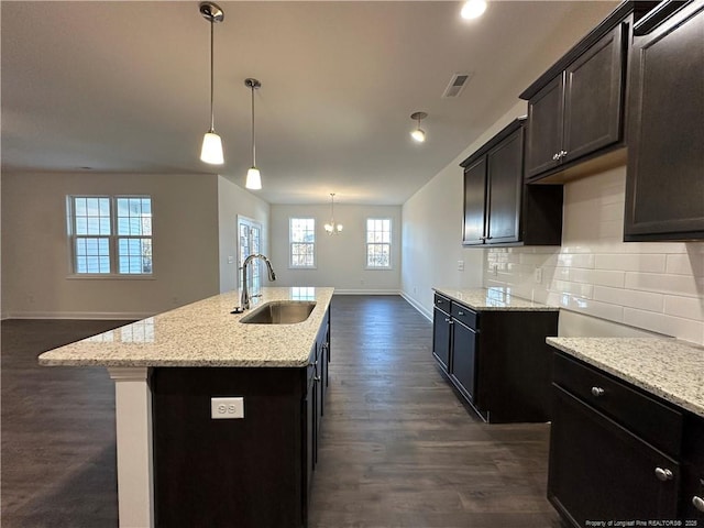 kitchen with pendant lighting, tasteful backsplash, sink, a kitchen island with sink, and light stone counters