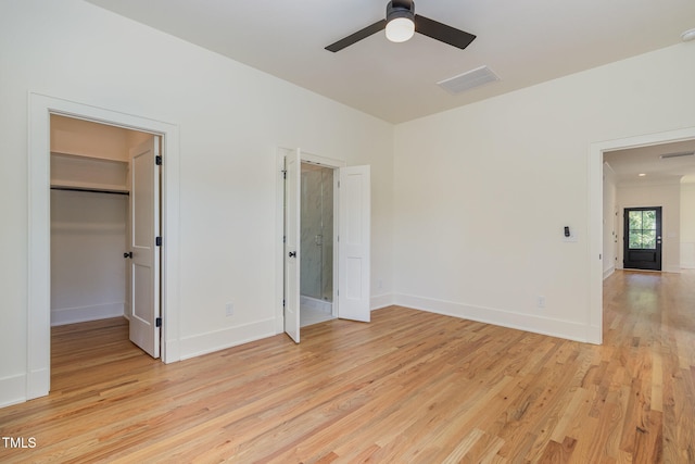 unfurnished bedroom featuring a closet, light wood-type flooring, a walk in closet, and ceiling fan