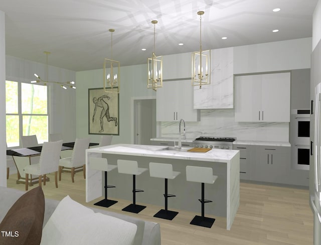 kitchen featuring a kitchen island with sink, sink, decorative light fixtures, light wood-type flooring, and white cabinets