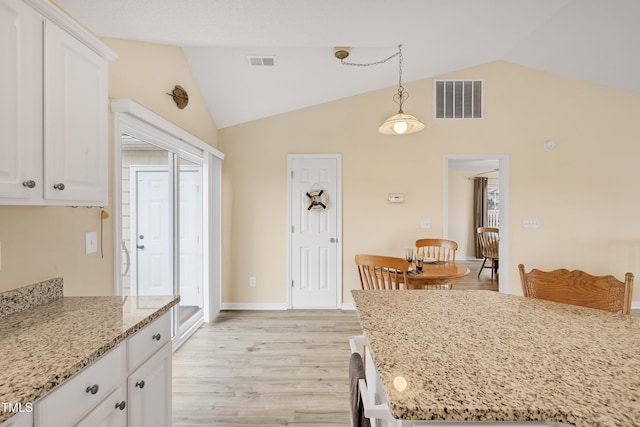 kitchen featuring light stone counters, decorative light fixtures, lofted ceiling, white cabinets, and light wood-type flooring