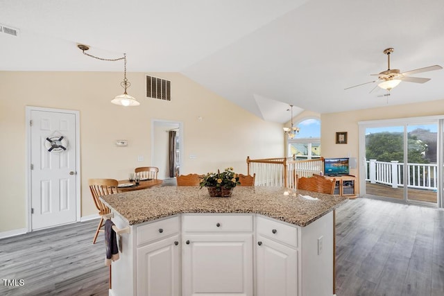 kitchen featuring lofted ceiling, light wood-type flooring, decorative light fixtures, a kitchen island, and white cabinetry