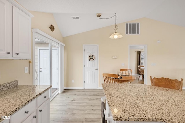 kitchen with white cabinets, light hardwood / wood-style floors, light stone countertops, and lofted ceiling