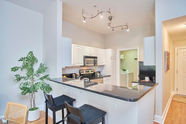 kitchen with light hardwood / wood-style floors, kitchen peninsula, white cabinets, and appliances with stainless steel finishes