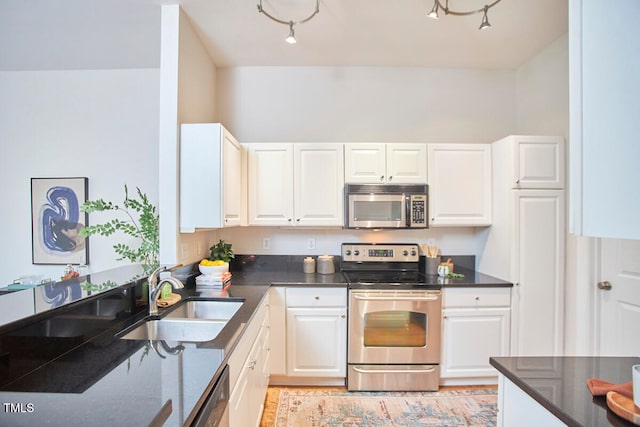 kitchen featuring appliances with stainless steel finishes, sink, white cabinets, and dark stone counters