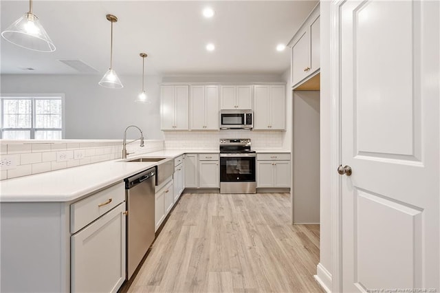 kitchen featuring white cabinetry, sink, hanging light fixtures, stainless steel appliances, and light hardwood / wood-style flooring