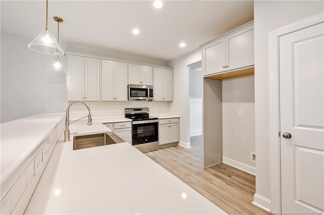 kitchen featuring stainless steel appliances, sink, white cabinets, and decorative light fixtures