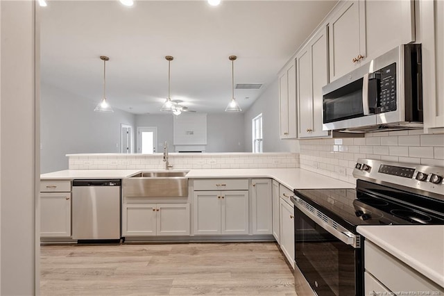 kitchen with sink, decorative light fixtures, light hardwood / wood-style flooring, appliances with stainless steel finishes, and white cabinets