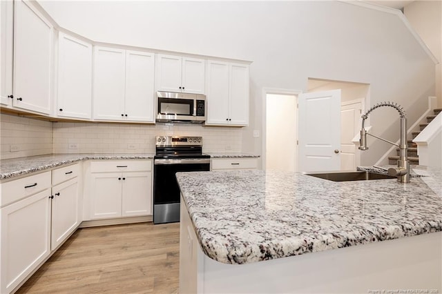 kitchen with stainless steel appliances, sink, white cabinets, and light stone counters