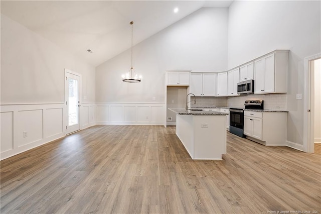 kitchen featuring appliances with stainless steel finishes, high vaulted ceiling, white cabinets, dark stone counters, and hanging light fixtures