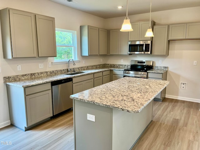 kitchen featuring pendant lighting, sink, appliances with stainless steel finishes, a center island, and light stone countertops