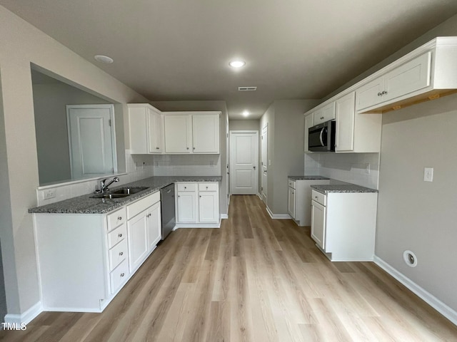 kitchen with stainless steel appliances, dark stone countertops, sink, white cabinetry, and light hardwood / wood-style floors