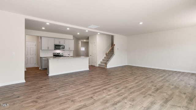 kitchen with light wood finished floors, an island with sink, gray cabinets, stainless steel appliances, and open floor plan