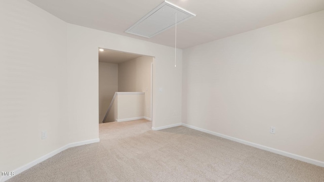 carpeted spare room featuring baseboards and attic access