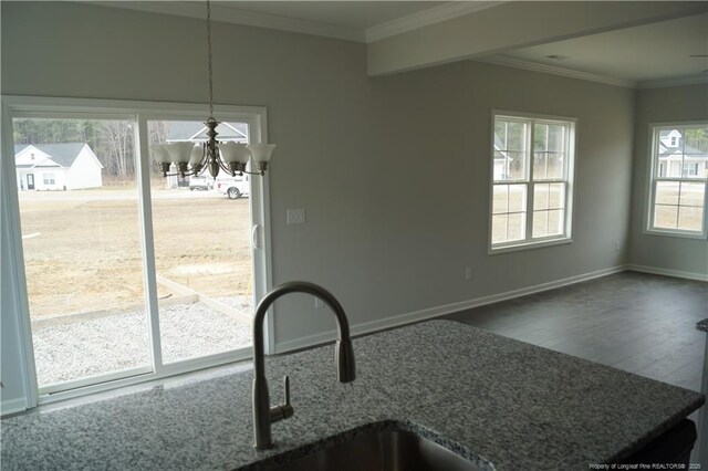 unfurnished dining area with a sink, wood finished floors, baseboards, ornamental molding, and an inviting chandelier