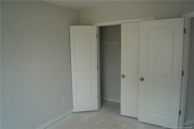 unfurnished bedroom featuring concrete floors, a closet, and baseboards