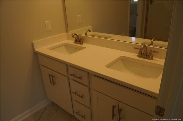 bathroom with double vanity, baseboards, a sink, and marble finish floor
