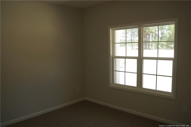 unfurnished room with baseboards, a wealth of natural light, and dark carpet