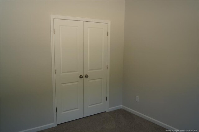 unfurnished bedroom with baseboards, a closet, and dark colored carpet