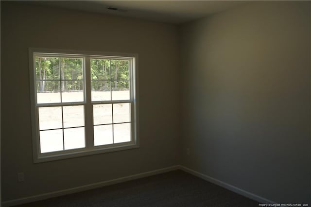 spare room featuring baseboards, dark carpet, and visible vents