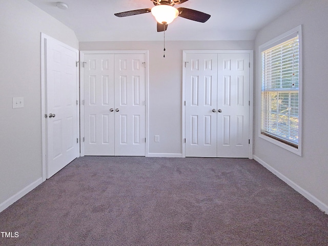 unfurnished bedroom with ceiling fan, dark colored carpet, and two closets