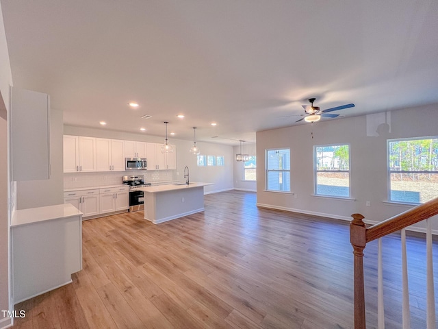 kitchen with appliances with stainless steel finishes, white cabinetry, backsplash, a kitchen island with sink, and decorative light fixtures