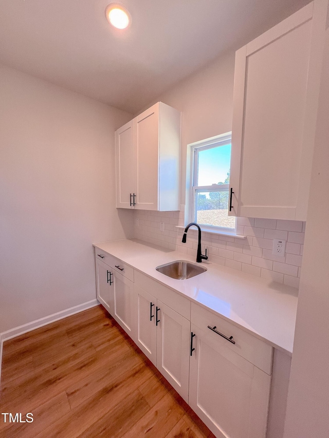 kitchen with sink, decorative backsplash, light hardwood / wood-style flooring, and white cabinets