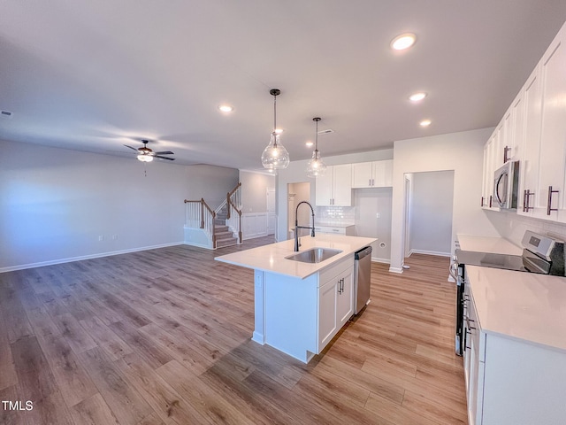 kitchen featuring pendant lighting, an island with sink, sink, white cabinets, and stainless steel appliances