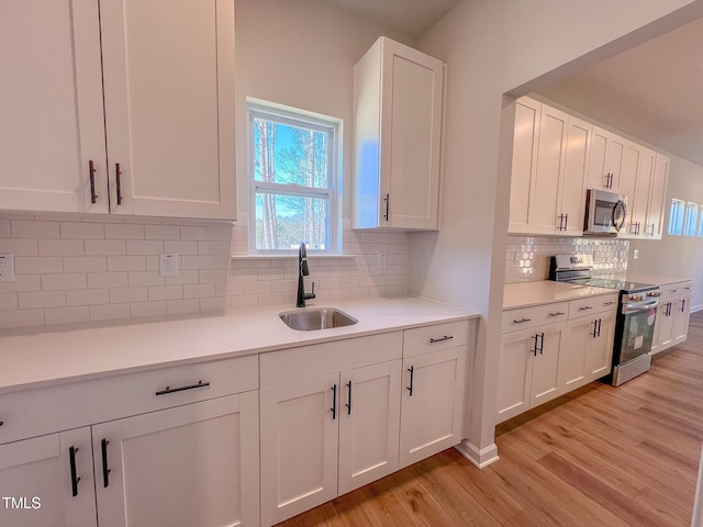 kitchen featuring white cabinetry, sink, backsplash, light hardwood / wood-style floors, and stainless steel appliances